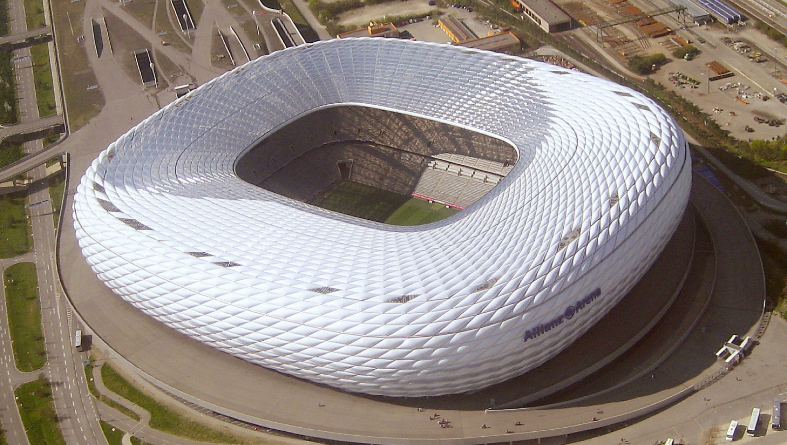An aerial photograph of the Allianz Arena in Munich, surrounded by roads and railway land.
