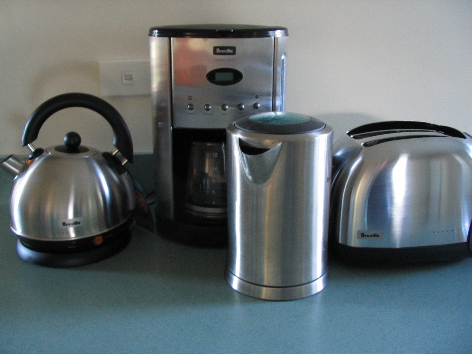 A casual snapshot of the four appliances crowded together on a blue worktop in front of a cream wall with a wall socket.
